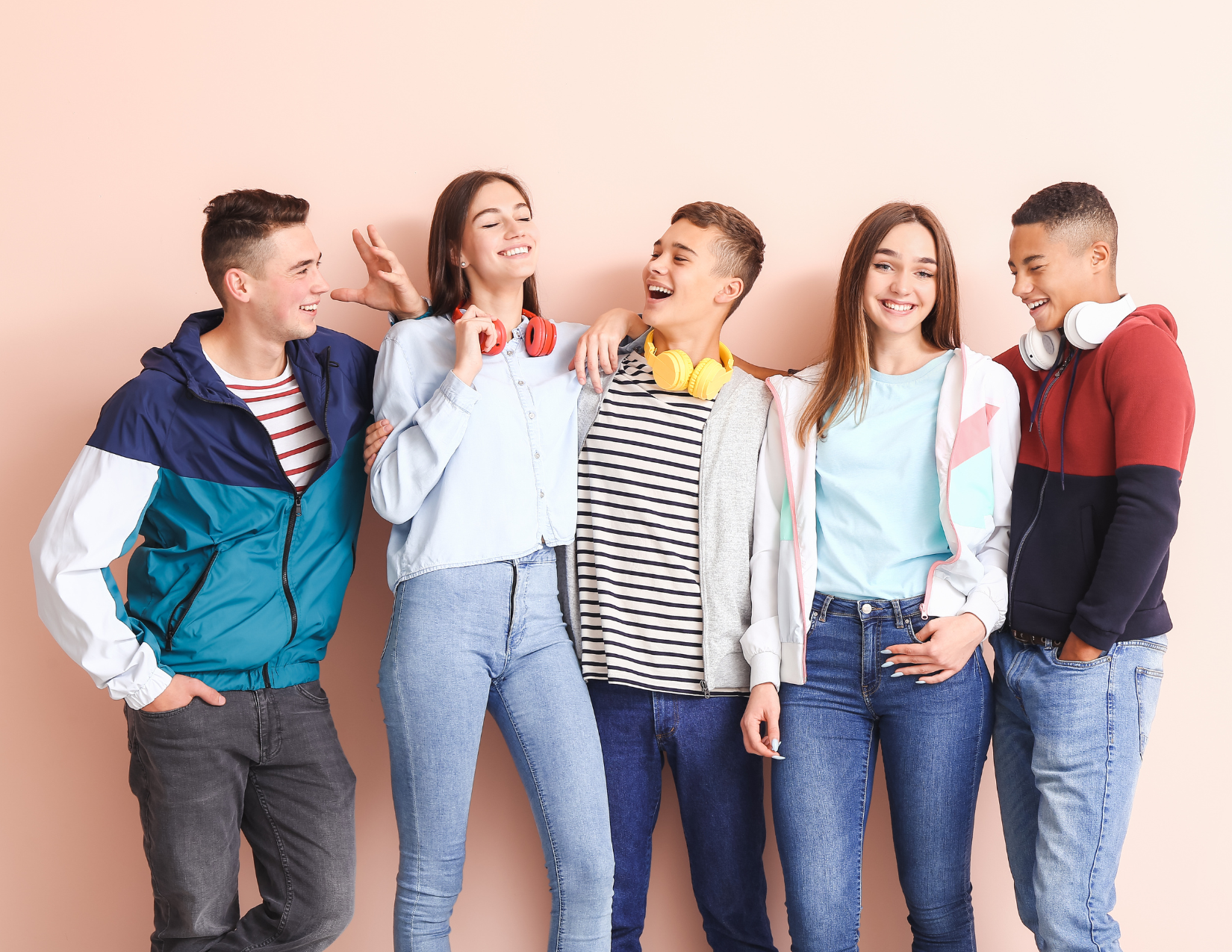 Five teens standing in front of a wall, smiling and chatting. 