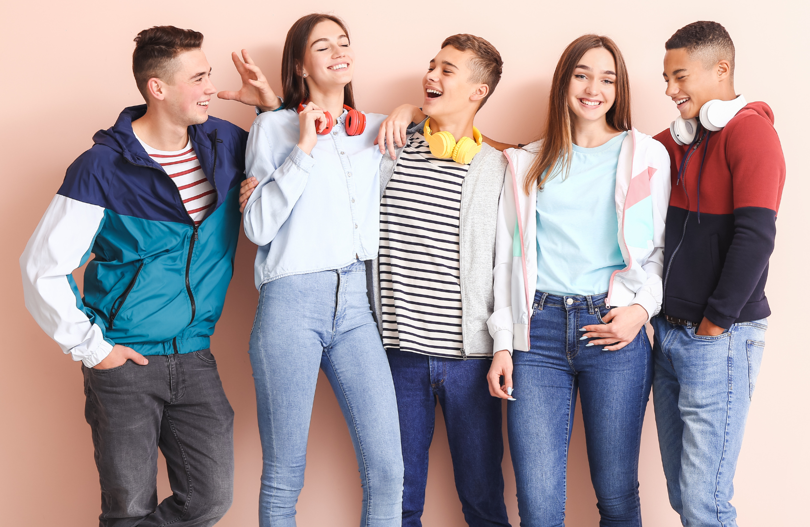 Five smiling teens standing next to a wall. 