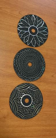 Three cd's painted black with white art designs. 