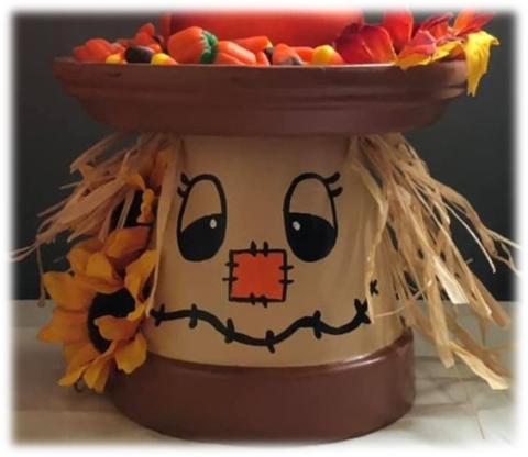 Upside down clay pot painted like a scarecrow with candy on a clay tray on top of his head.