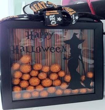 Black shadowbox filled with orange glitter pumpkins and black witch on the glass. 