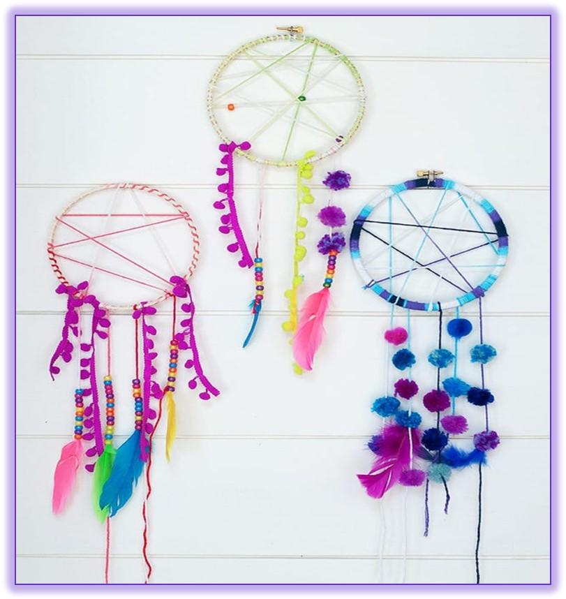 Three dream catchers in pink, blue and yellow. Feathers and beads attached to each dream catcher. 