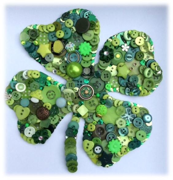 Green four leaf clover made from buttons on blue background.