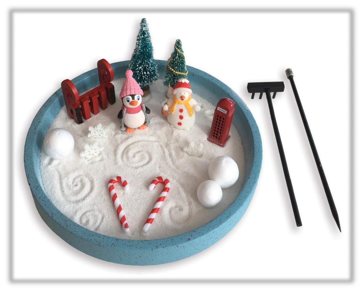 Blue container filled with white sand. Penguin and snowman with three snowballs and two candy canes. A couple of trees and a bench. Rake and pick next to it. 